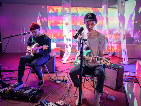 Jesse Maranger and Chris Minielly performing and playing their guitars, purple, yellow, red, orange and pink lights flash and project in the background