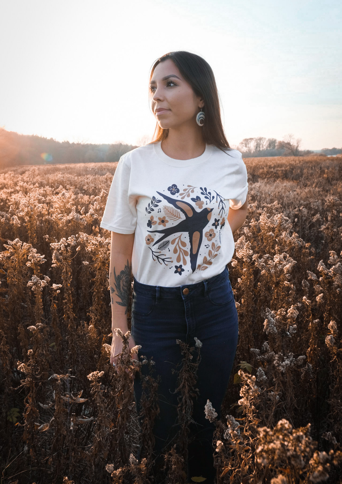 A girl wearing a white shirt with a bird pattern standing outside in the bushes