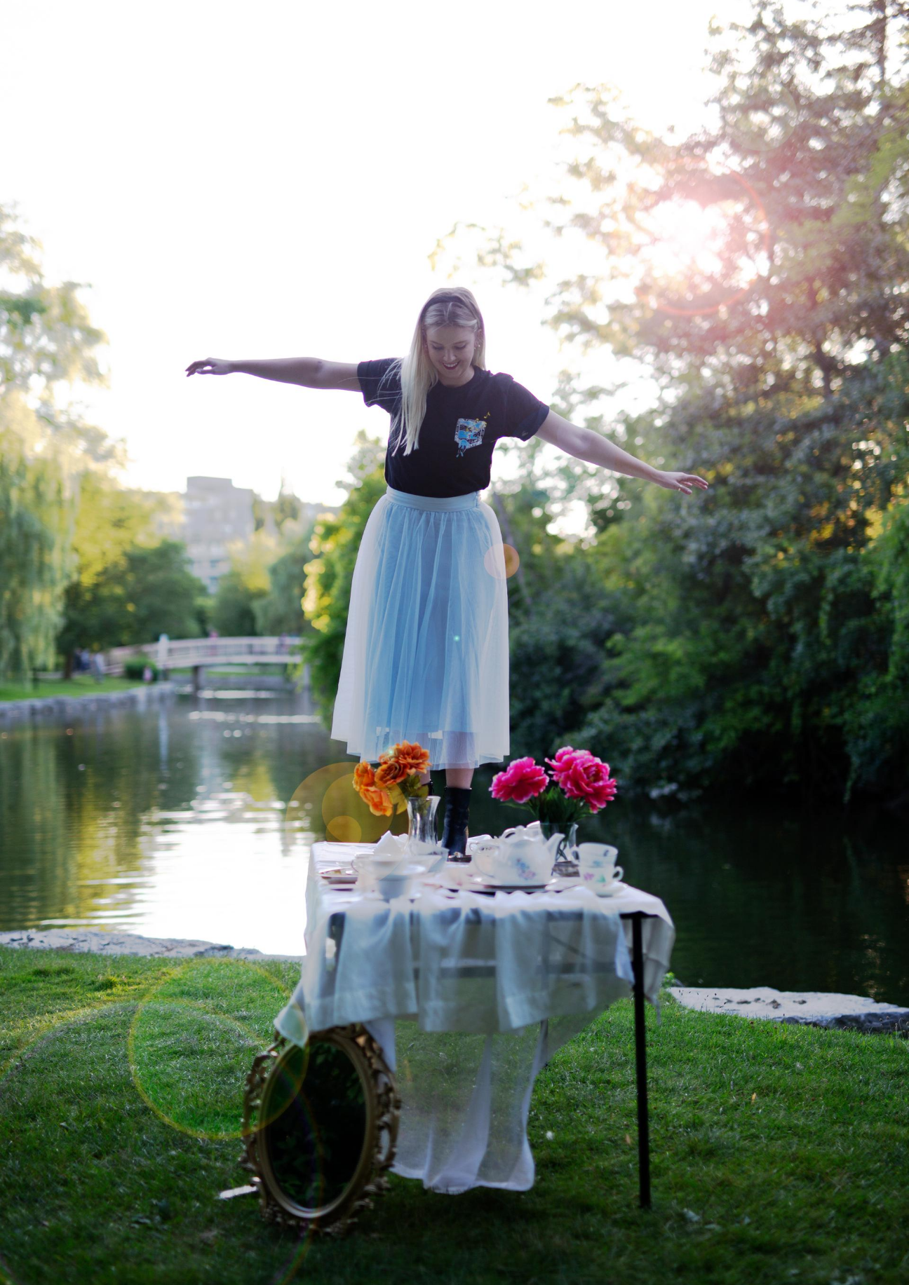 girl wearing black limited run t-shirt standing on top of a table with flowers in a parkl