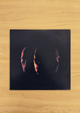 vinyl cover art of 3 masks side by side on a black cover on a wooden background