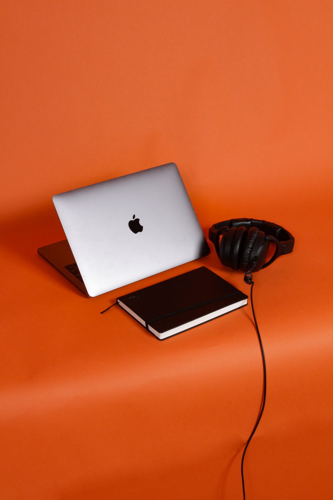 laptop, book and headphones with orange back drop