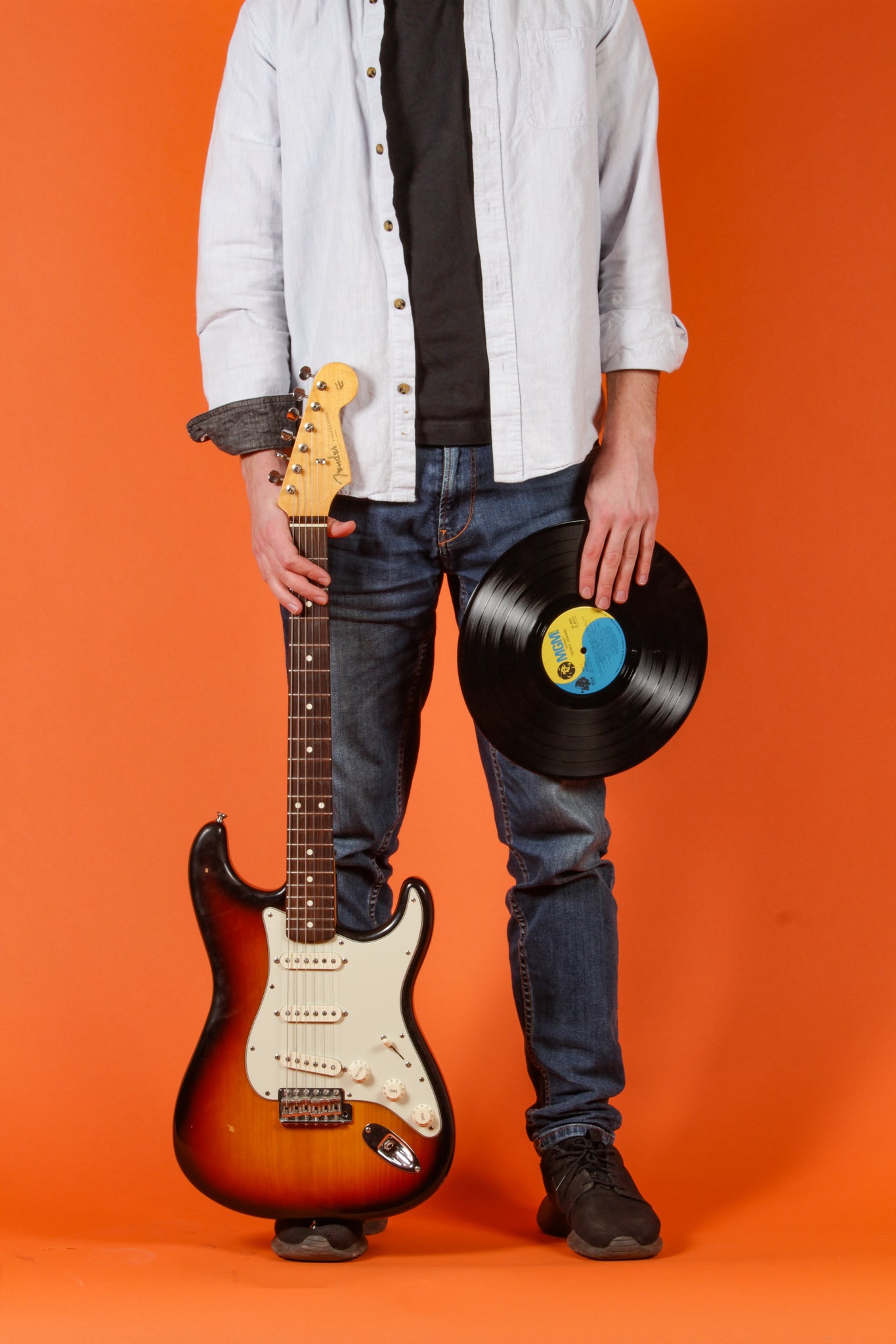 person holding a guitar and a record standing in front of an orange background