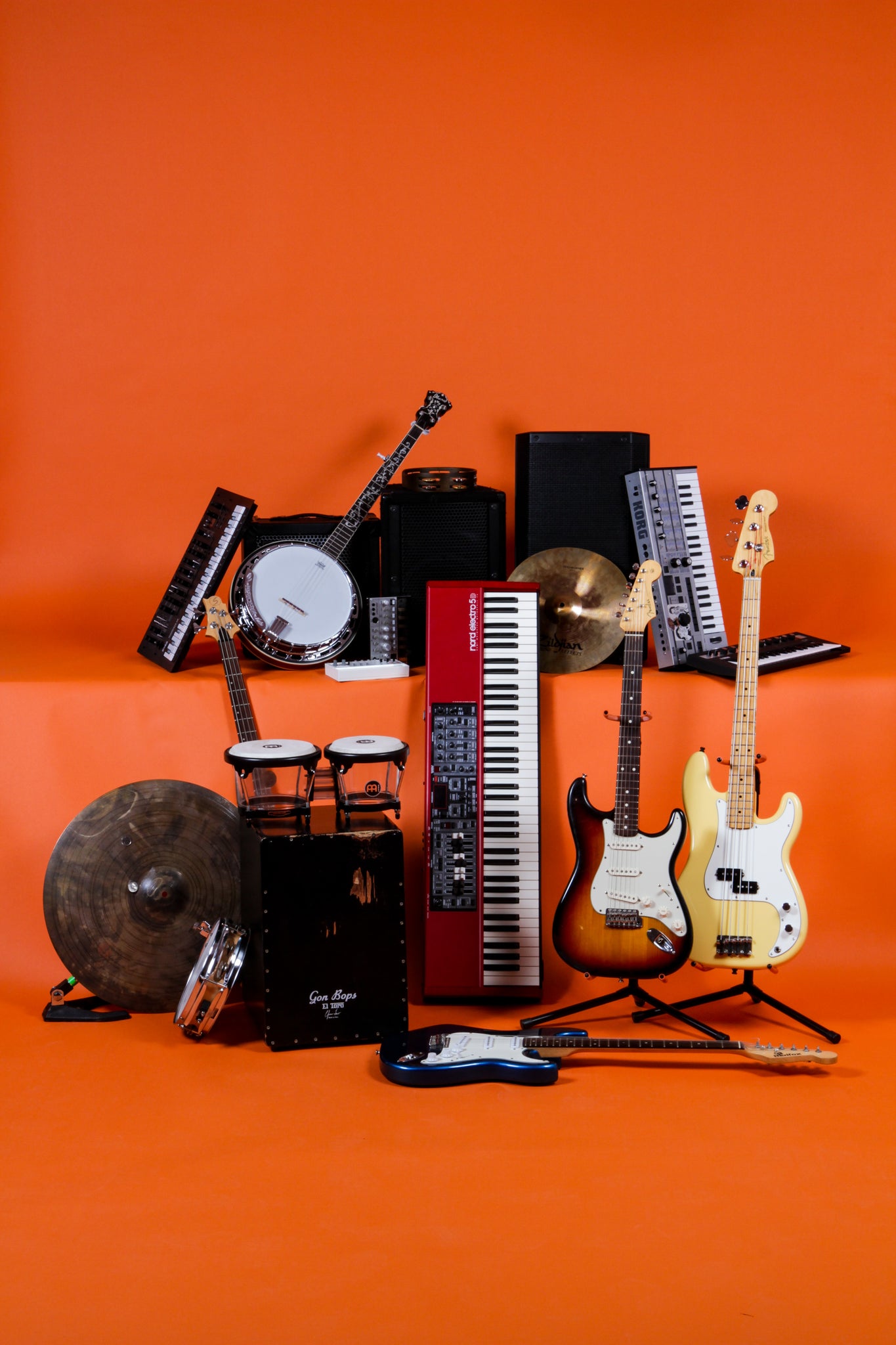 keyboards, guitars, amps, percussion instruments arranged in front of an orange background