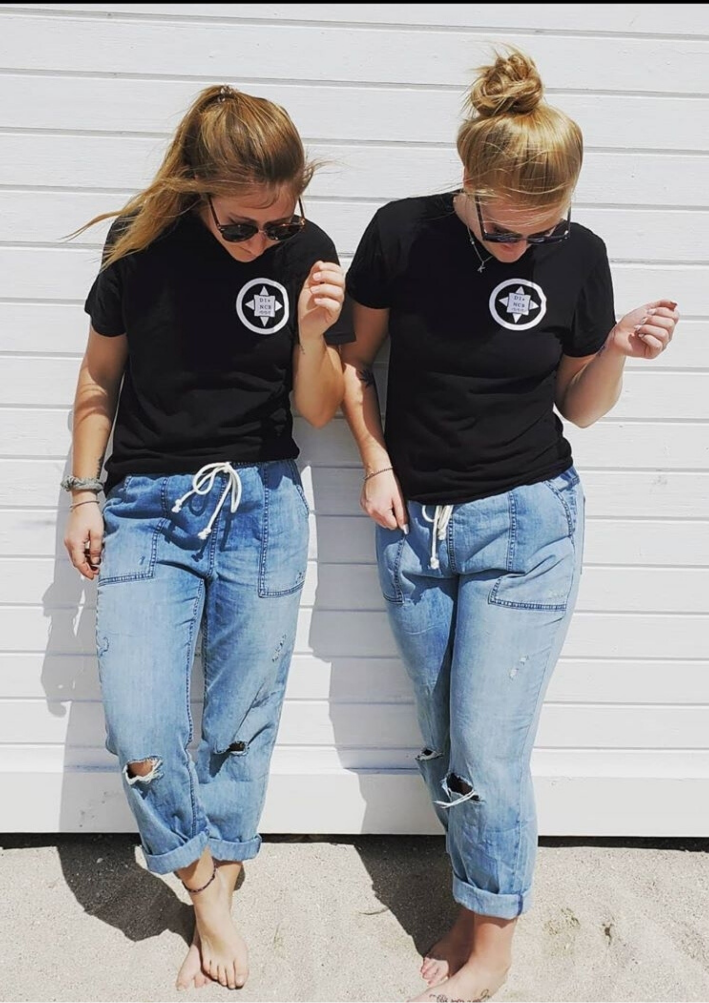 two girls wearing black North Coast Logo T-Shirts standing in front of a white back drop